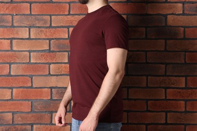 Photo of Young man wearing stylish brown t-shirt near brick wall, closeup. Mockup for design