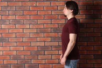 Photo of Young man wearing stylish brown t-shirt near brick wall. Mockup for design