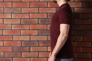 Photo of Young man wearing stylish brown t-shirt near brick wall, closeup. Mockup for design