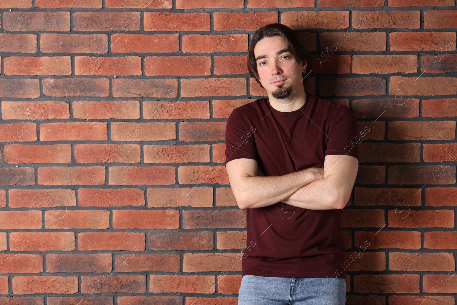 Photo of Young man wearing stylish brown t-shirt near brick wall. Mockup for design