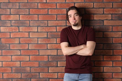 Photo of Young man wearing stylish brown t-shirt near brick wall. Mockup for design