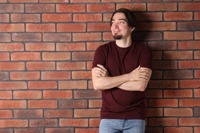 Photo of Young man wearing stylish brown t-shirt near brick wall. Mockup for design