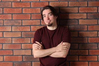 Photo of Young man wearing stylish brown t-shirt near brick wall. Mockup for design