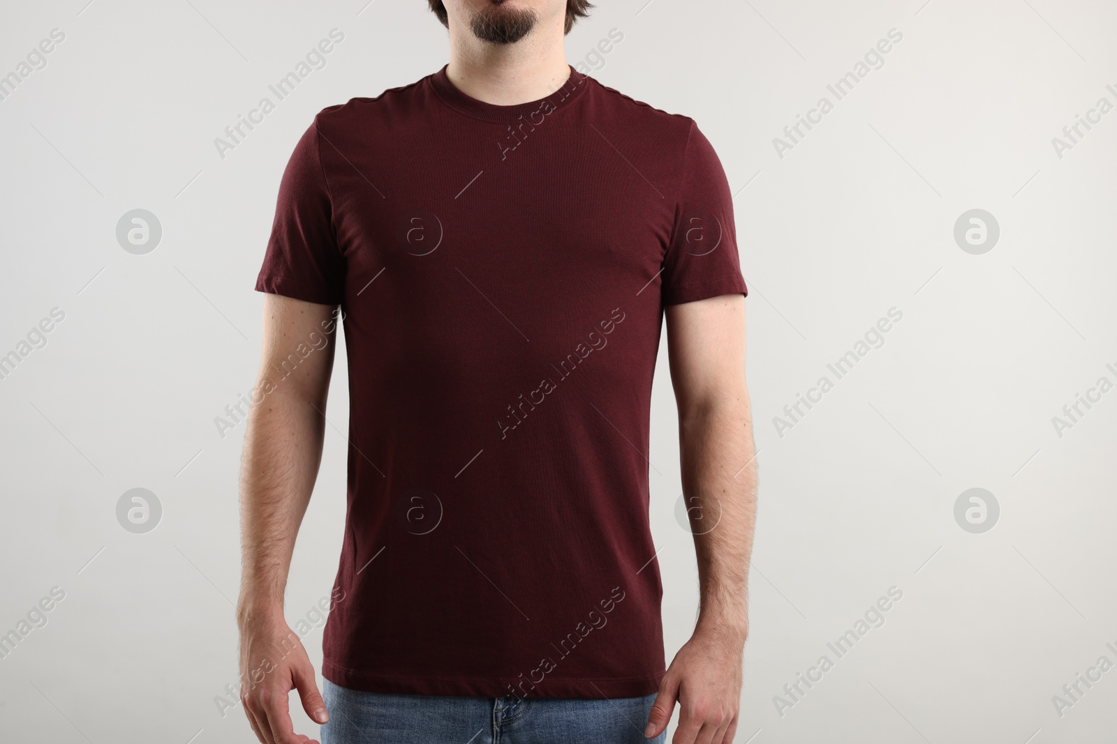Photo of Young man wearing stylish brown t-shirt near light grey background, closeup. Mockup for design