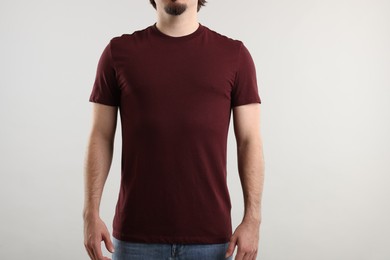 Photo of Young man wearing stylish brown t-shirt near light grey background, closeup. Mockup for design