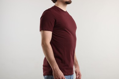 Photo of Young man wearing stylish brown t-shirt near light grey background, closeup. Mockup for design