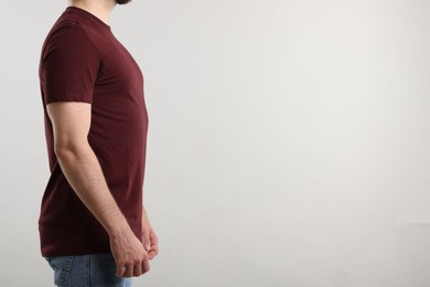 Photo of Young man wearing stylish brown t-shirt near light grey background, closeup. Mockup for design