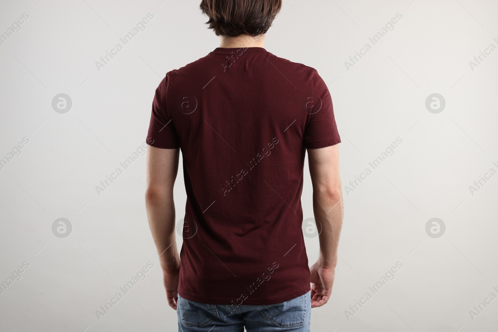 Photo of Young man wearing stylish brown t-shirt near light grey background, back view. Mockup for design