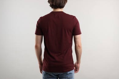 Photo of Young man wearing stylish brown t-shirt near light grey background, back view. Mockup for design