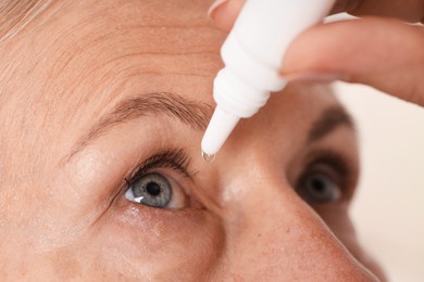 Photo of Woman applying eye drops on light background, closeup