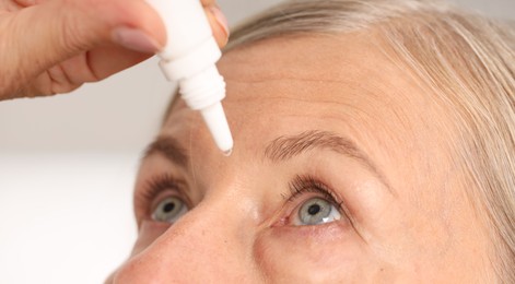Photo of Woman applying eye drops on light background, closeup