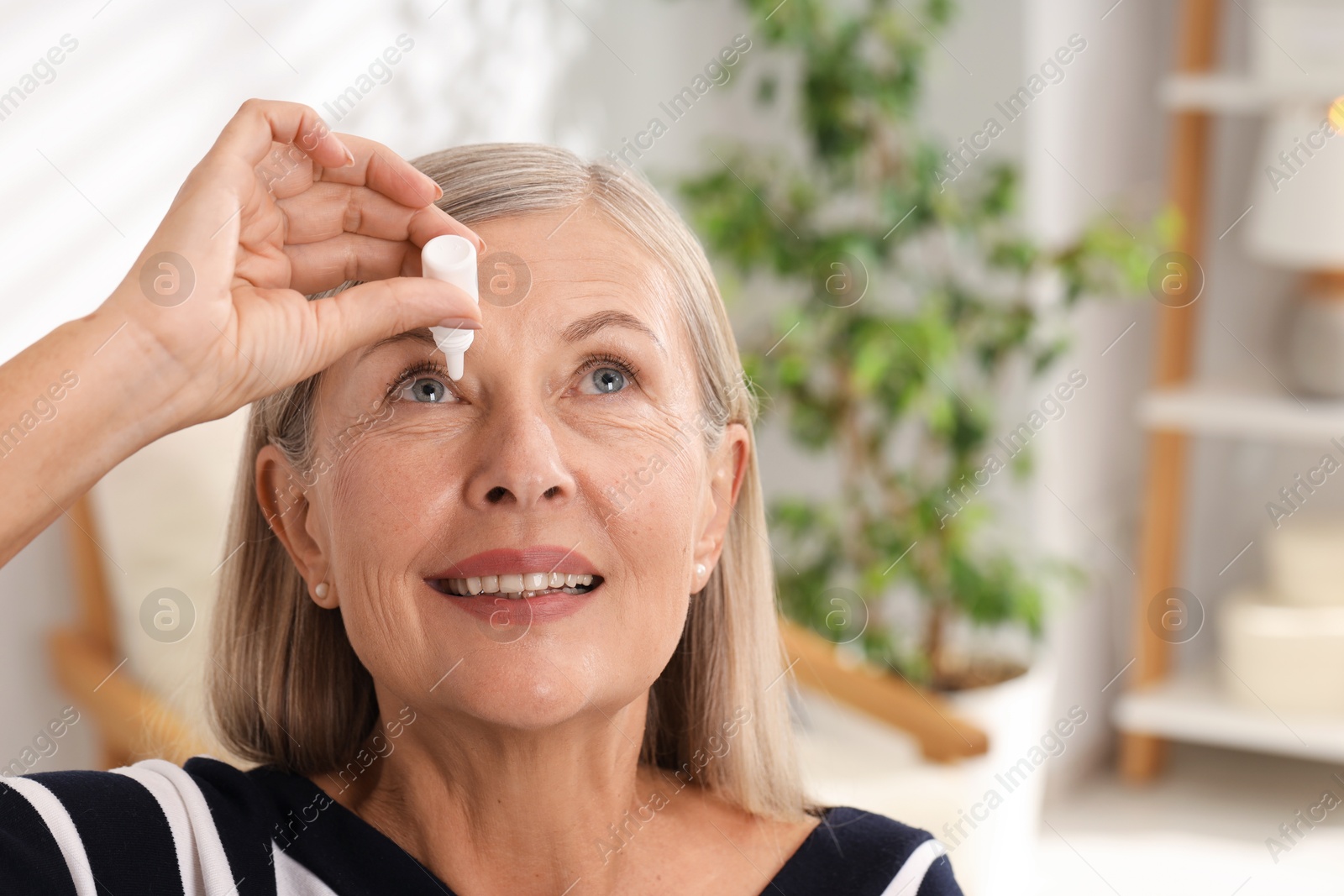 Photo of Senior woman applying eye drops at home. Space for text