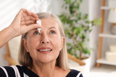 Photo of Senior woman applying eye drops at home. Space for text
