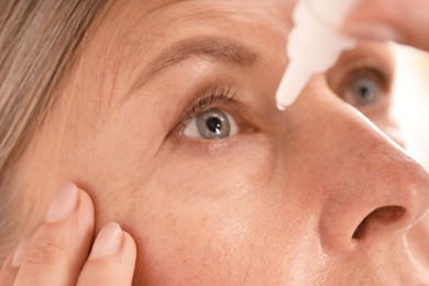 Photo of Woman applying eye drops on light background, closeup