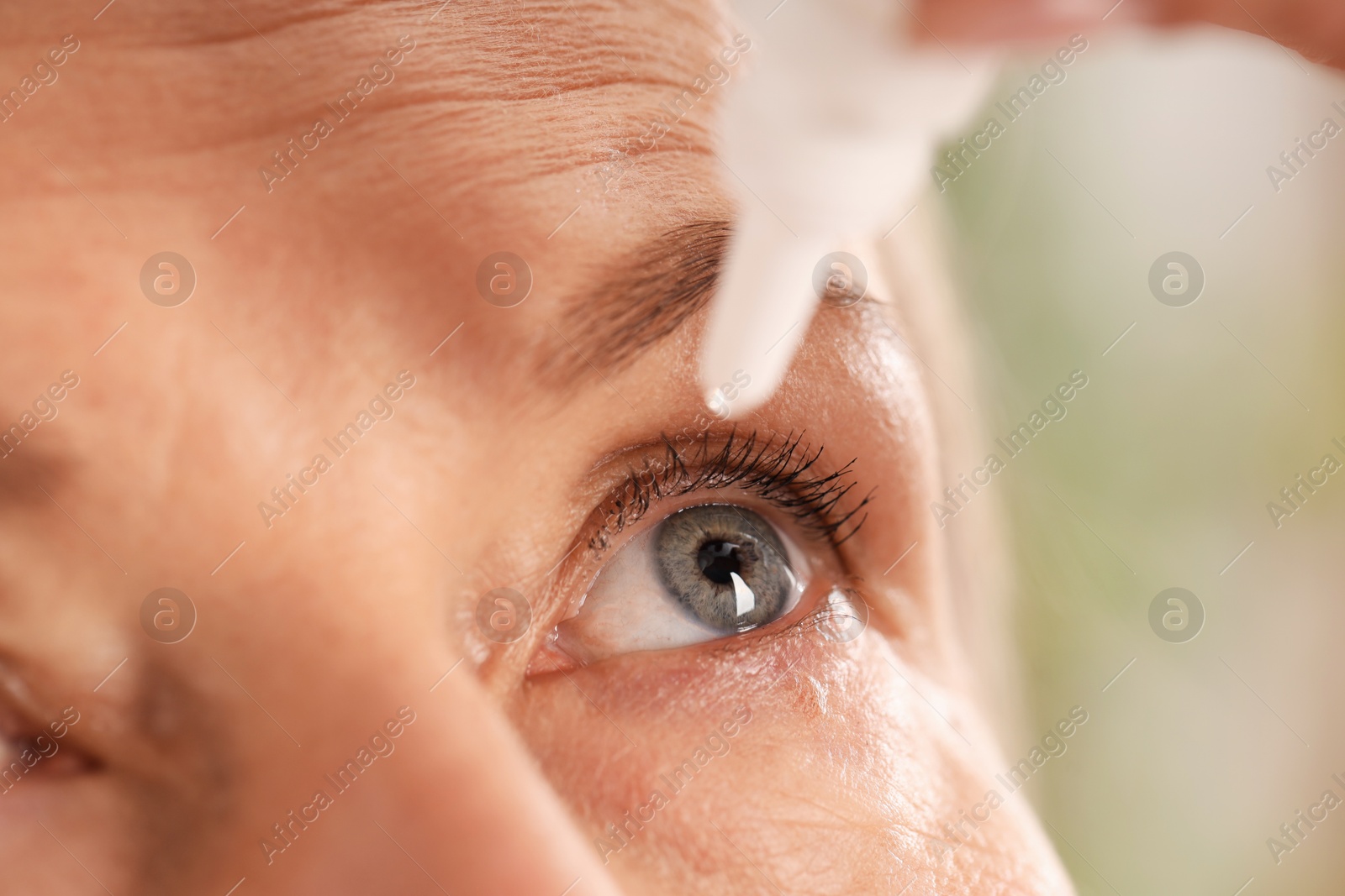 Photo of Woman applying eye drops on blurred background, closeup