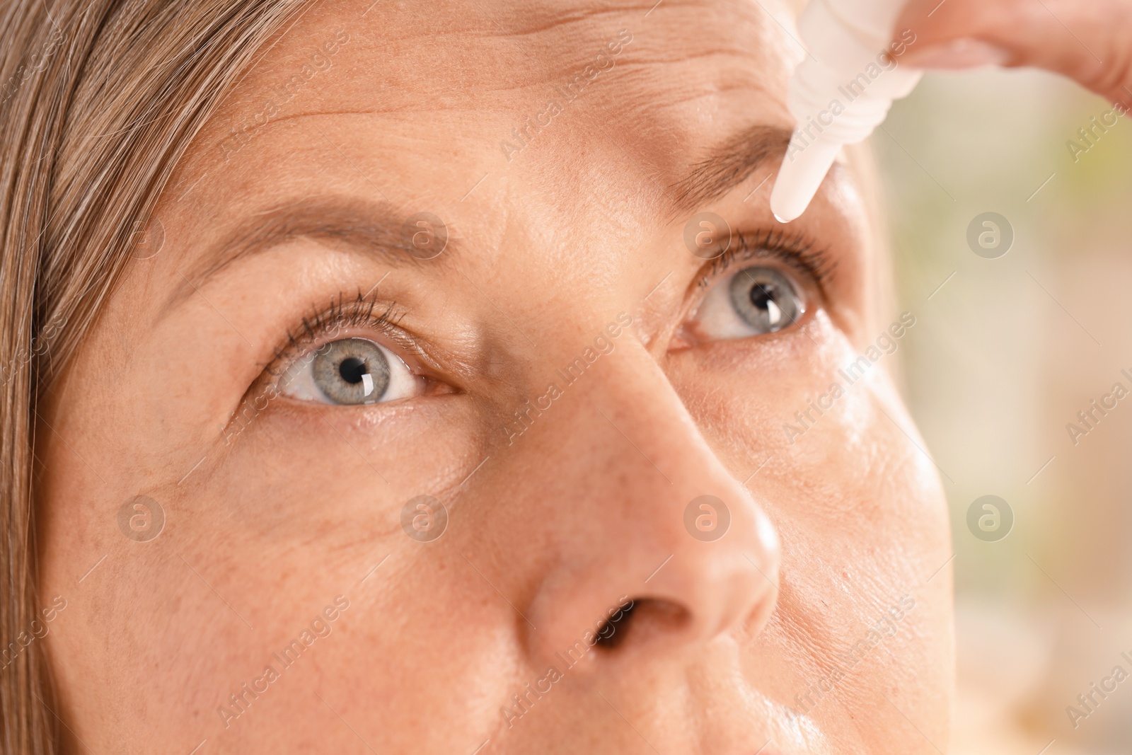 Photo of Woman applying eye drops on blurred background, closeup