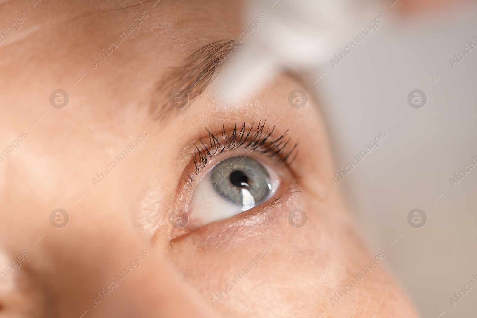 Photo of Woman applying eye drops on blurred background, closeup