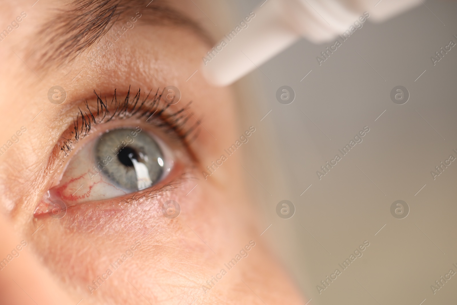 Photo of Woman applying eye drops on blurred background, closeup