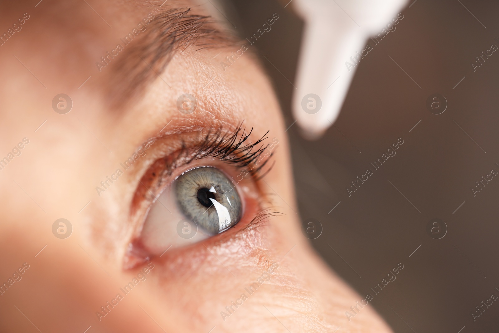 Photo of Woman applying eye drops on blurred background, closeup