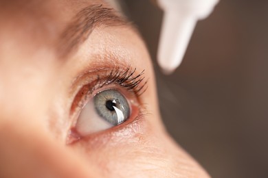 Photo of Woman applying eye drops on blurred background, closeup