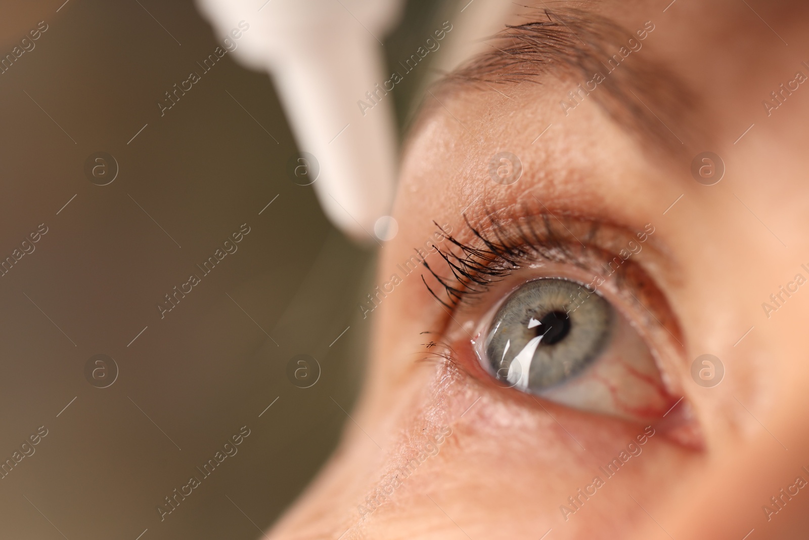 Photo of Woman applying eye drops on blurred background, closeup