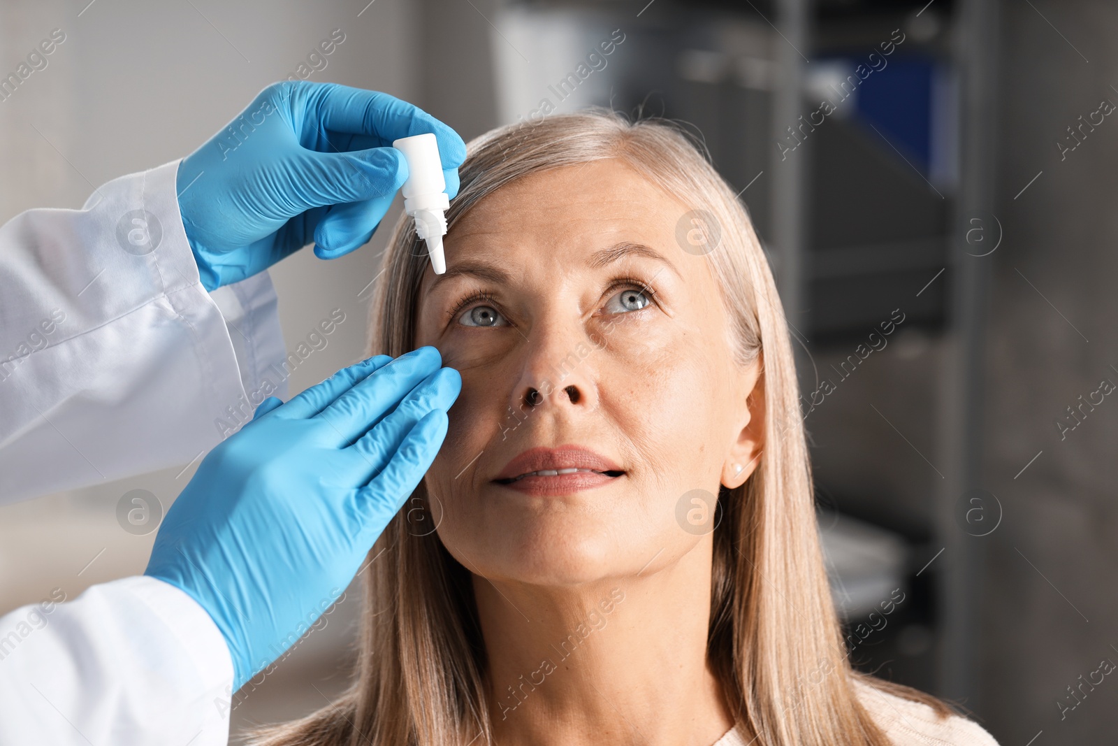 Photo of Doctor putting drops into woman's eye indoors, closeup
