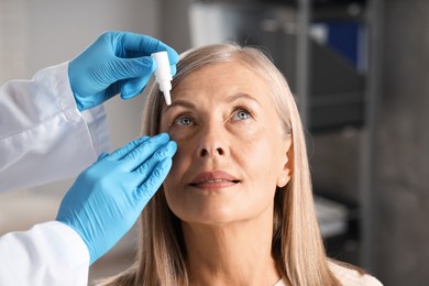 Photo of Doctor putting drops into woman's eye indoors, closeup