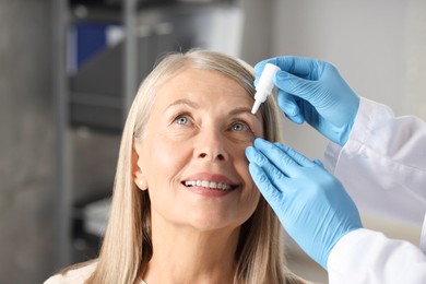 Photo of Doctor putting drops into woman's eye indoors, closeup