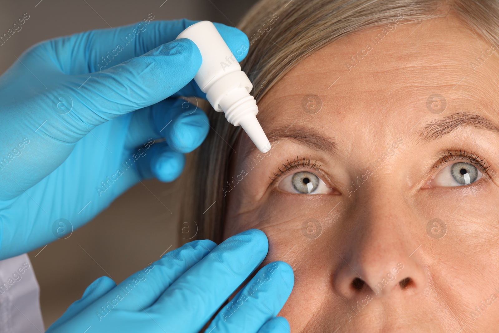 Photo of Doctor putting drops into woman's eye indoors, closeup