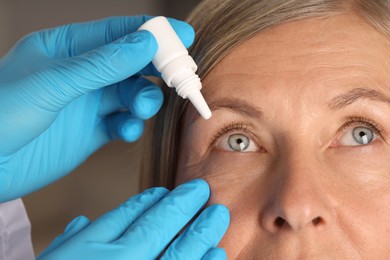 Photo of Doctor putting drops into woman's eye indoors, closeup