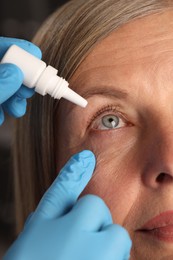 Photo of Doctor putting drops into woman's eye indoors, closeup