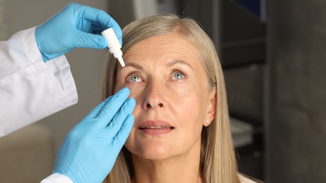 Photo of Doctor putting drops into woman's eye indoors, closeup