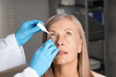 Photo of Doctor putting drops into woman's eye indoors, closeup