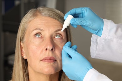 Photo of Doctor putting drops into woman's eye indoors, closeup