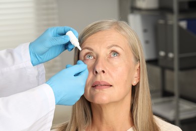 Photo of Doctor putting drops into woman's eye indoors, closeup
