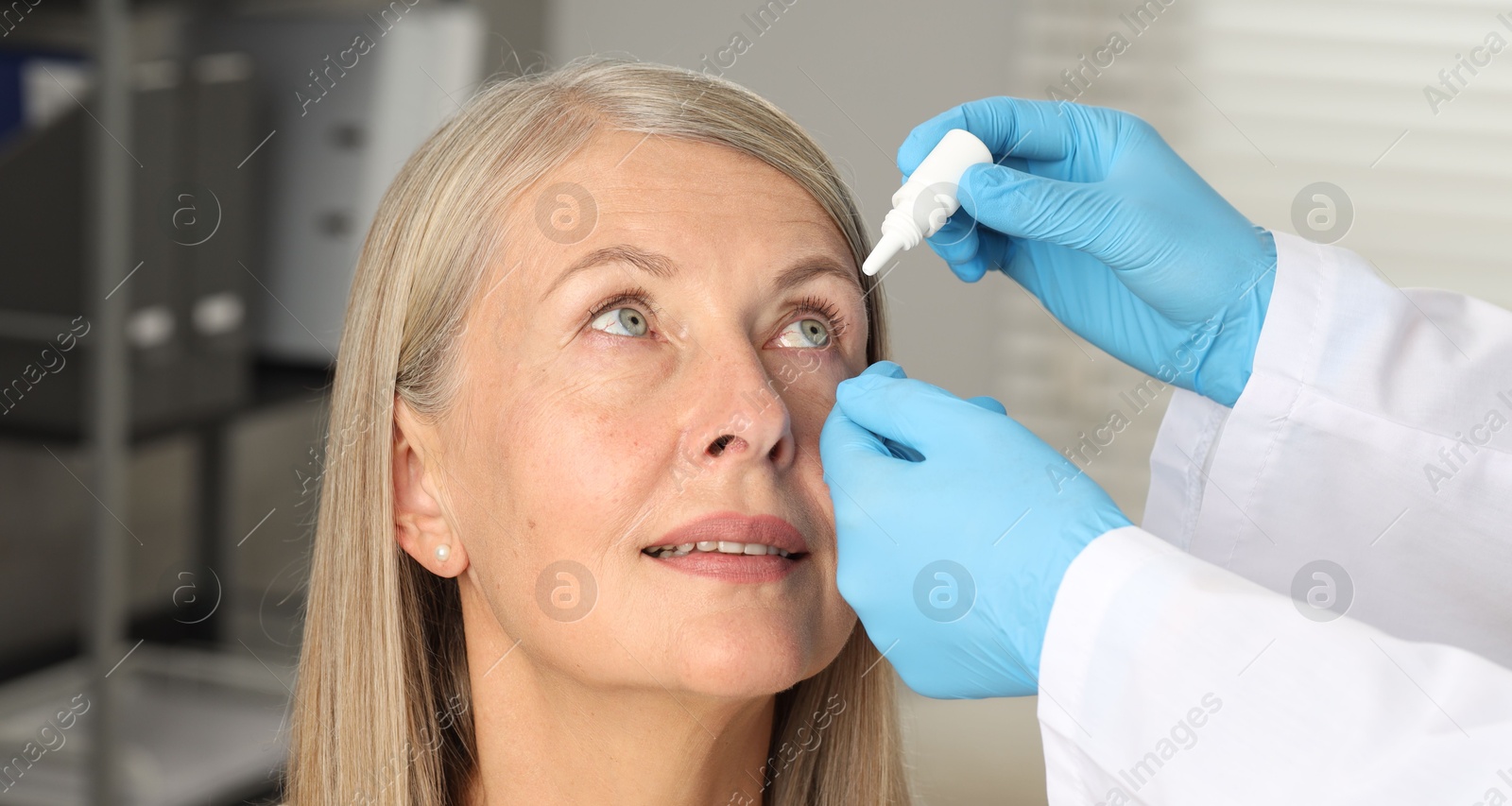 Photo of Doctor putting drops into woman's eye indoors, closeup