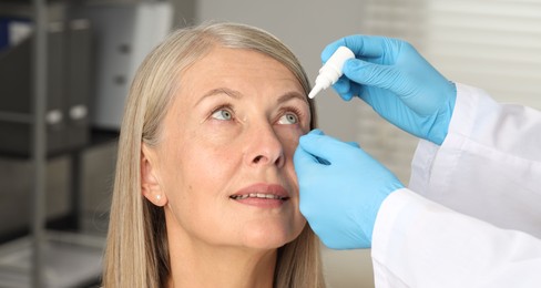 Photo of Doctor putting drops into woman's eye indoors, closeup