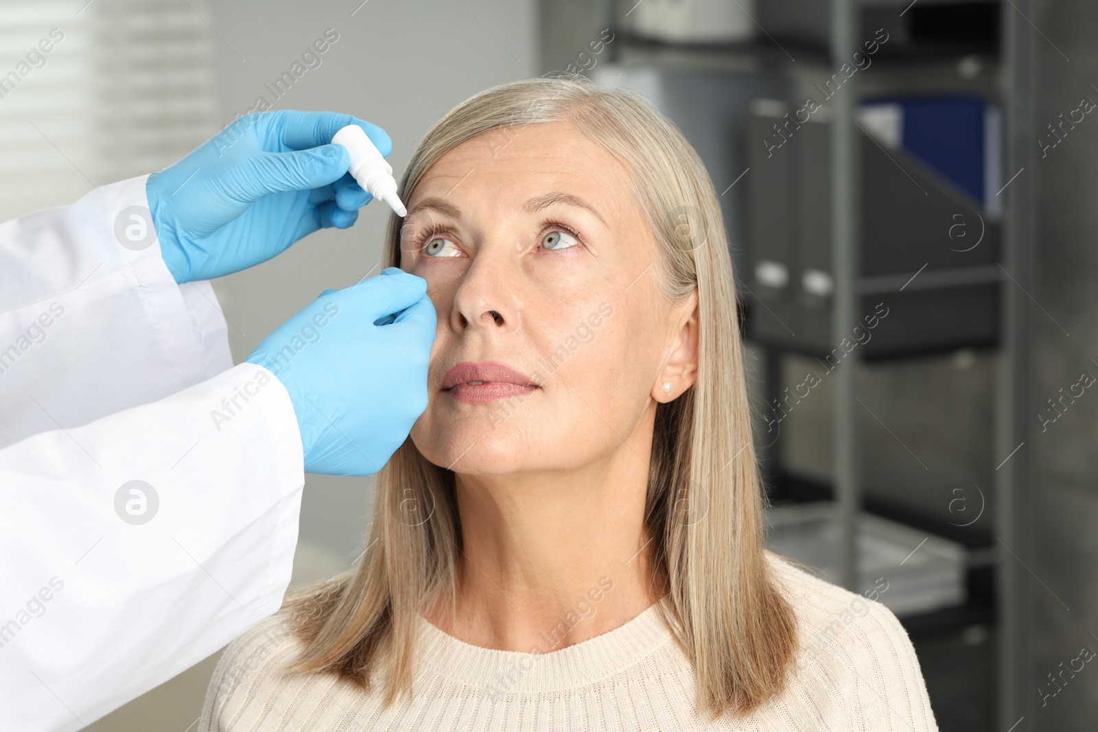 Photo of Doctor putting drops into woman's eye indoors, closeup