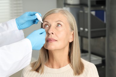 Photo of Doctor putting drops into woman's eye indoors, closeup