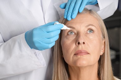 Photo of Doctor putting drops into woman's eye indoors, closeup