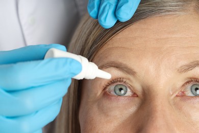 Photo of Doctor putting drops into woman's eye indoors, closeup