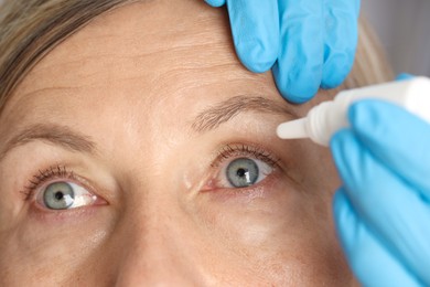 Photo of Doctor putting drops into woman's eye indoors, closeup
