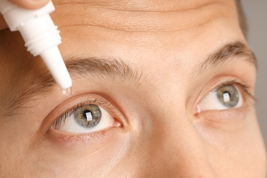Photo of Man applying eye drops on grey background, closeup