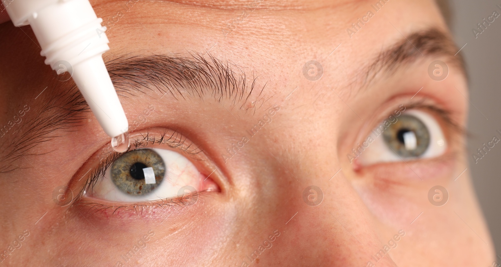 Photo of Man applying eye drops on grey background, closeup