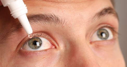 Photo of Man applying eye drops on grey background, closeup