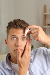 Photo of Young man applying eye drops at home