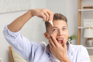 Photo of Young man applying eye drops at home