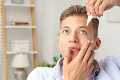 Photo of Young man applying eye drops at home. Space for text