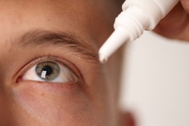 Photo of Man applying eye drops on light background, closeup