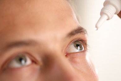 Photo of Man applying eye drops on light background, closeup